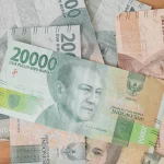 Ilustrasi lembaran rupiah pecahan 20.000 dan 5.000 di atas meja kayu