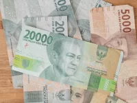 Ilustrasi lembaran rupiah pecahan 20.000 dan 5.000 di atas meja kayu