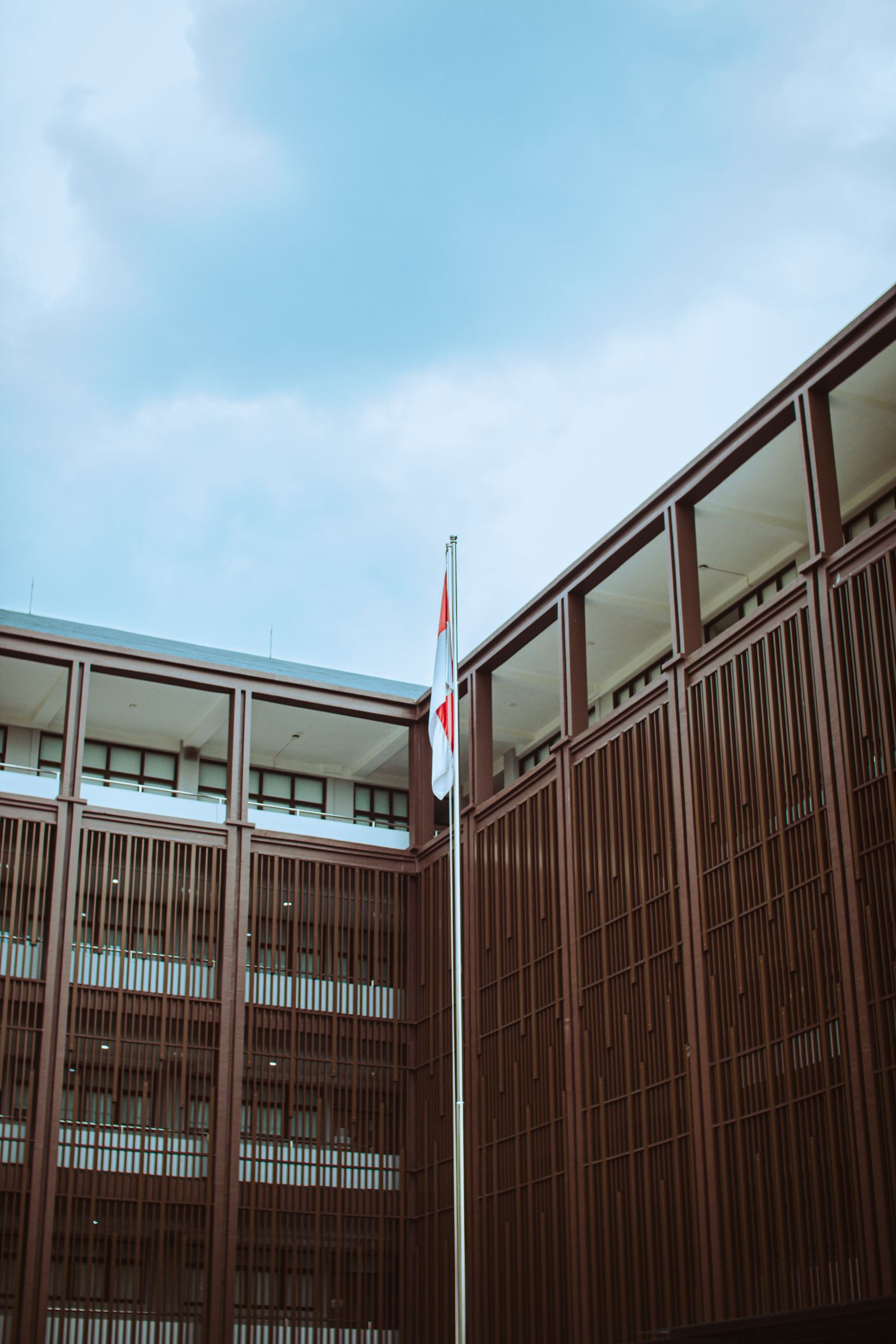Ilustrasi gedung perkantoran modern dengan bendera Merah Putih berkibar di halaman.