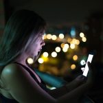 Ilustrasi seorang perempuan menatap layar telepon genggam pada malam hari.