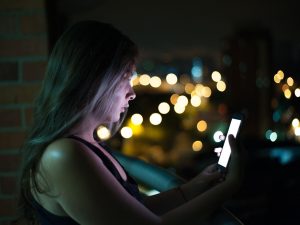 Ilustrasi seorang perempuan menatap layar telepon genggam pada malam hari.