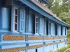 Dinding kayu masjid berwarna biru dengan panel ukiran bercat emas dan latar pepohonan