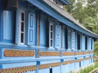 Dinding kayu masjid berwarna biru dengan panel ukiran bercat emas dan latar pepohonan