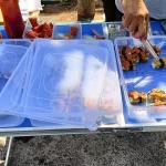 Tangan pedagang menjepit sushi dari nampan plastik di lapak kaki lima Jombang
