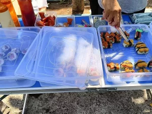 Tangan pedagang menjepit sushi dari nampan plastik di lapak kaki lima Jombang
