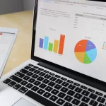Layar laptop menampilkan grafik dan bagan data di atas meja kerja