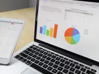 Layar laptop menampilkan grafik dan bagan data di atas meja kerja
