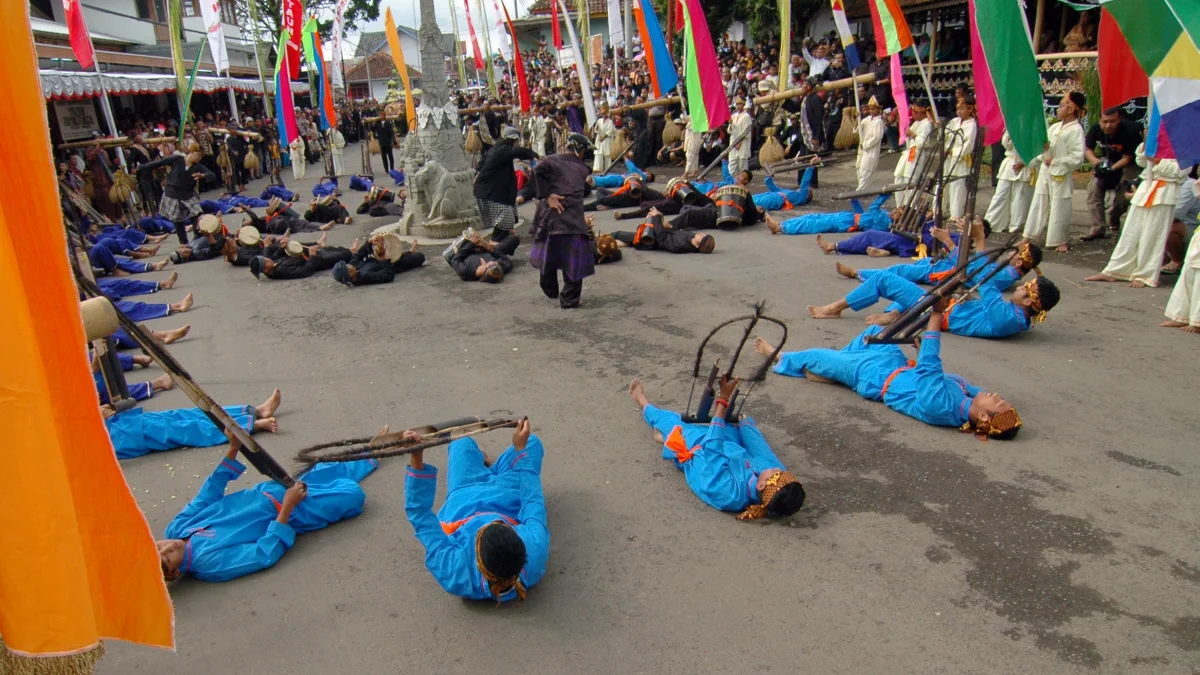 Penampil berbaring di jalan dengan alat musik bambu dalam arak-arakan Seren Taun, Cigugur, Kuningan