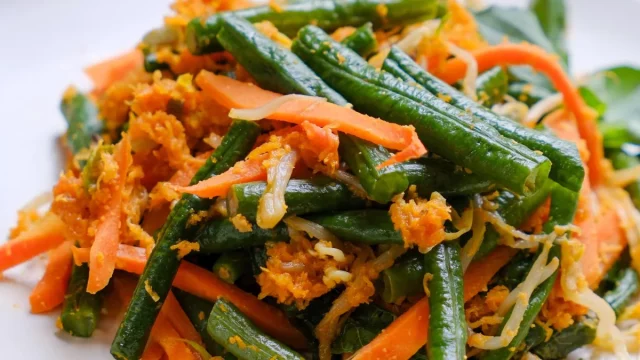 Urap kacang panjang, wortel, dan tauge berbalut kelapa parut berbumbu di atas piring putih