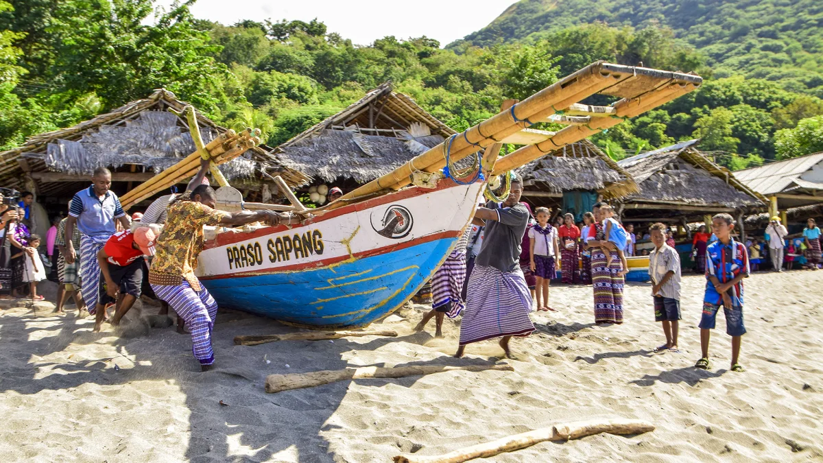 Warga Lamalera mendorong perahu peledang di pantai berpasir, disaksikan anak-anak dan warga