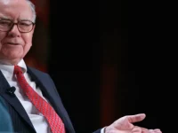 Warren Buffett mengenakan jas gelap dan dasi merah saat berbicara di sebuah acara