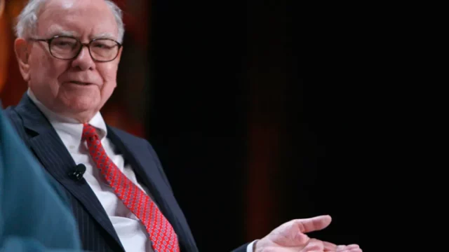 Warren Buffett mengenakan jas gelap dan dasi merah saat berbicara di sebuah acara