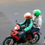Pengemudi ojek daring berhelm oranye membonceng penumpang berhelm hijau di jalan