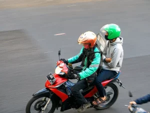 Pengemudi ojek daring berhelm oranye membonceng penumpang berhelm hijau di jalan