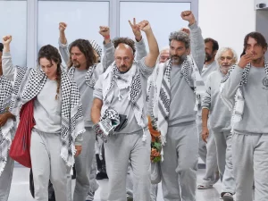 Aktivis Global Sumud Flotilla berseragam abu-abu mengepalkan tangan saat tiba di bandara Roma