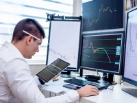 Seorang pria memantau grafik harga saham di tablet dan beberapa monitor