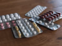Ilustrasi beberapa strip tablet dan kapsul obat tergeletak di atas meja kayu