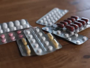 Ilustrasi beberapa strip tablet dan kapsul obat tergeletak di atas meja kayu