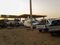 Ilustrasi truk bak, mobil, dan minibus mengantre di depan SPBU saat senja di Sudan