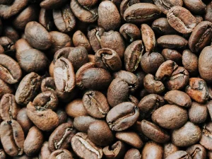 Hamparan biji kopi sangrai berwarna cokelat tua memenuhi seluruh bidang gambar