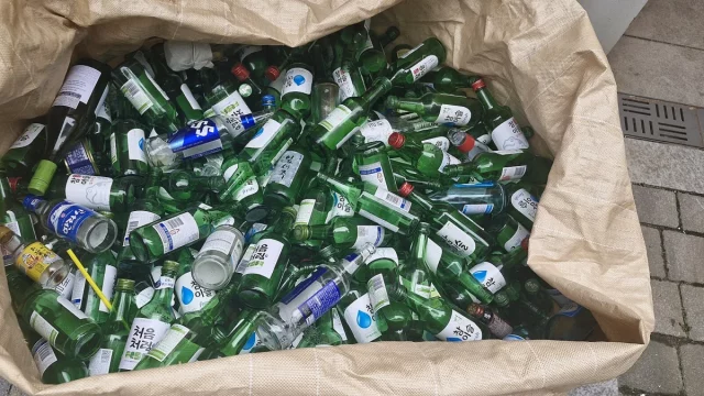 Ilustrasi tumpukan botol soju hijau kosong dalam karung daur ulang kaca di Korea Selatan