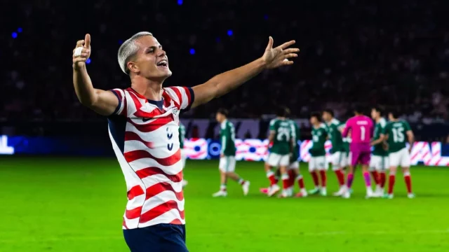 Cavan Sullivan merentangkan kedua tangan di lapangan dengan seragam bergaris merah putih timnas Amerika Serikat