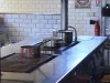 Ilustrasi dapur komersial kosong dengan meja dan kompor baja nirkarat, panci, serta dinding keramik putih