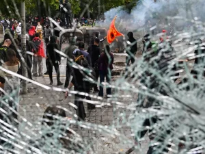 Demonstran antipemerintah terlihat dari balik kaca toko yang pecah di Tirana, Albania