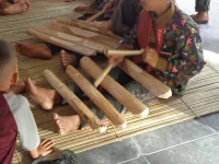 Ilustrasi bilah canang kayu Singkil dijejerkan di atas kaki pemain dan dipukul dengan pemukul kayu