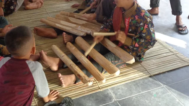 Ilustrasi bilah canang kayu Singkil dijejerkan di atas kaki pemain dan dipukul dengan pemukul kayu