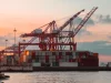 Derek merah dan tumpukan peti kemas di dermaga pelabuhan saat senja