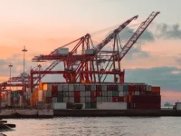 Derek merah dan tumpukan peti kemas di dermaga pelabuhan saat senja