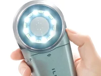 Ilustrasi tangan menggenggam dermatoskop dengan lingkar lampu LED menyala di sekeliling lensa