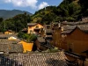 Ilustrasi atap genting dan rumah tua berdinding tanah di desa tradisional Tiongkok berlatar bukit berhutan