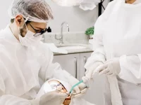 Ilustrasi dokter gigi bermasker bersama asisten menangani gigi pasien yang berbaring