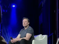 Elon Musk duduk di atas panggung dalam sebuah acara