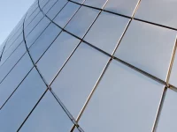 Panel kaca melengkung pada fasad gedung memantulkan langit biru