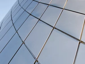 Panel kaca melengkung pada fasad gedung memantulkan langit biru