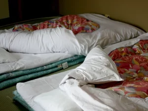 Kasur futon dengan selimut kusut di atas tatami kamar ryokan di Nara, Jepang