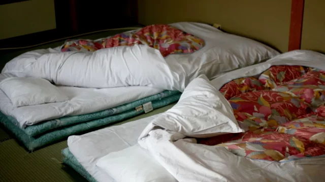 Kasur futon dengan selimut kusut di atas tatami kamar ryokan di Nara, Jepang