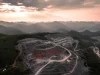 Ilustrasi foto udara tambang terbuka berundak di perbukitan karst berhutan saat senja