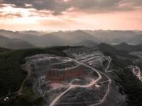 Ilustrasi foto udara tambang terbuka berundak di perbukitan karst berhutan saat senja