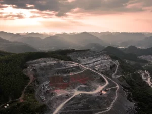 Ilustrasi foto udara tambang terbuka berundak di perbukitan karst berhutan saat senja