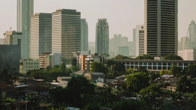 Deretan gedung perkantoran bertingkat Jakarta menjulang di atas permukiman padat berpohon
