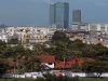 Gedung pencakar langit menjulang di atas permukiman beratap merah dan pepohonan rindang