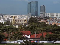 Gedung pencakar langit menjulang di atas permukiman beratap merah dan pepohonan rindang