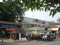 Ilustrasi gerbang dan gedung Rumah Sakit Mahosot dengan tuk-tuk terparkir di depannya, Vientiane, Laos