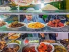 Penjual berjilbab melayani pembeli di balik etalase warung berisi aneka lauk matang