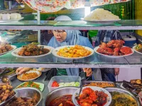 Penjual berjilbab melayani pembeli di balik etalase warung berisi aneka lauk matang