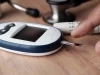 Ilustrasi glukometer dengan strip uji berdarah dan alat tusuk jari di meja kayu